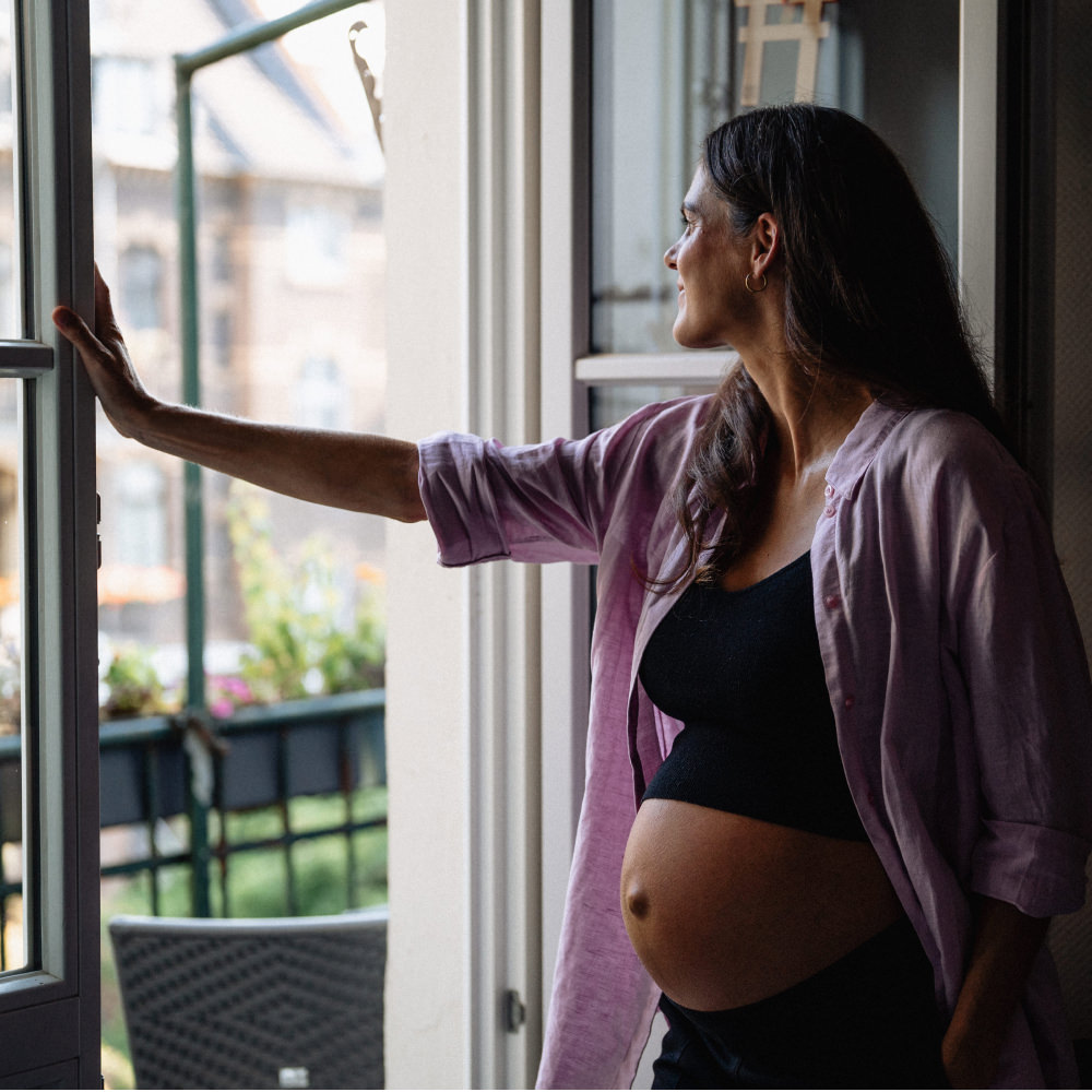 Schwanger Frau steht am Fenster