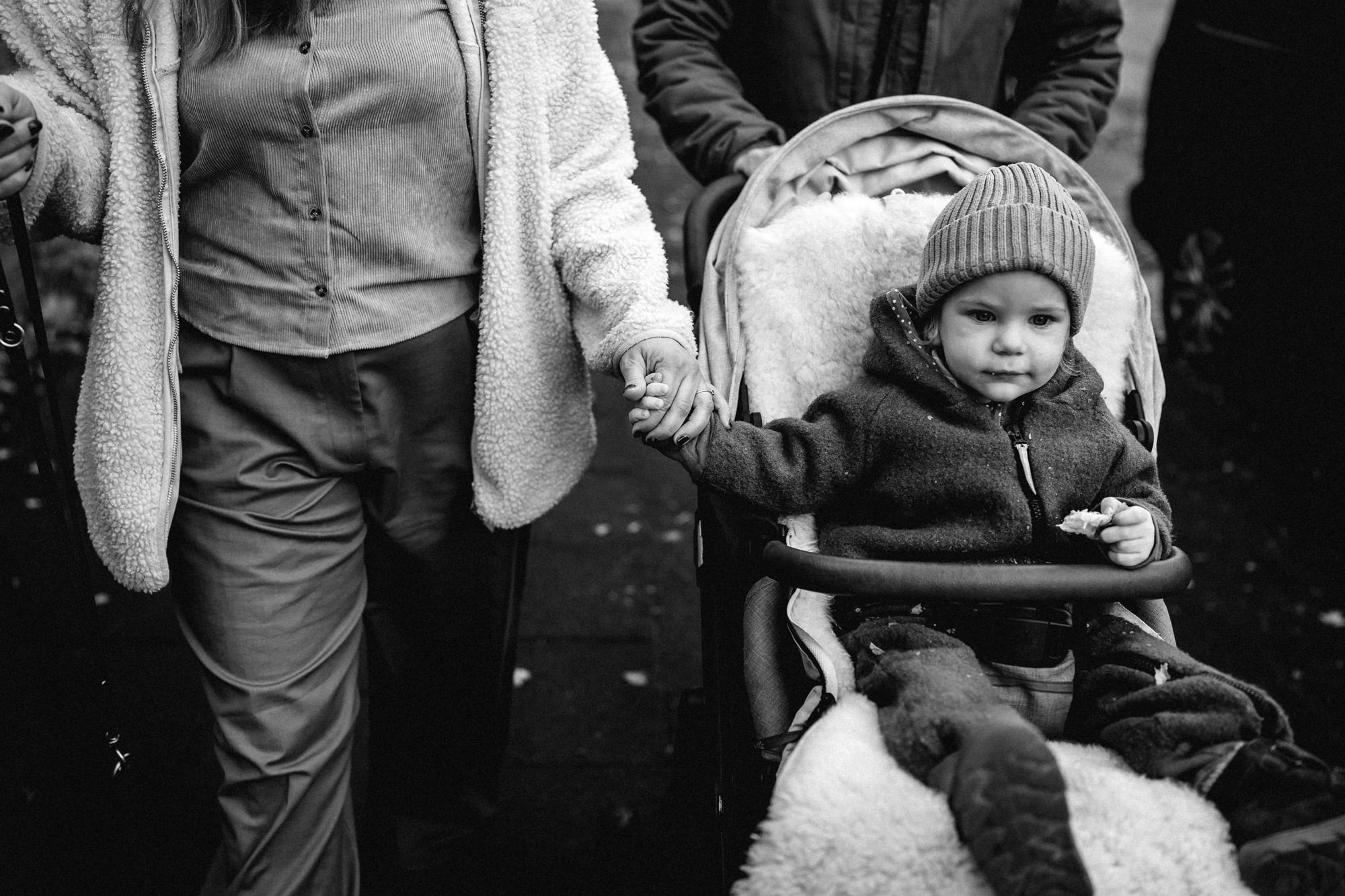 Kind sitzt im Kinderwagen und hält die Hand der Mutter
