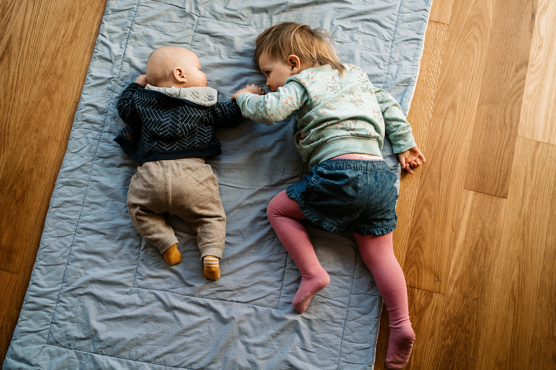 Zwei Geschwister liegen nebeneinander auf einer Decke im Wohnzimmer