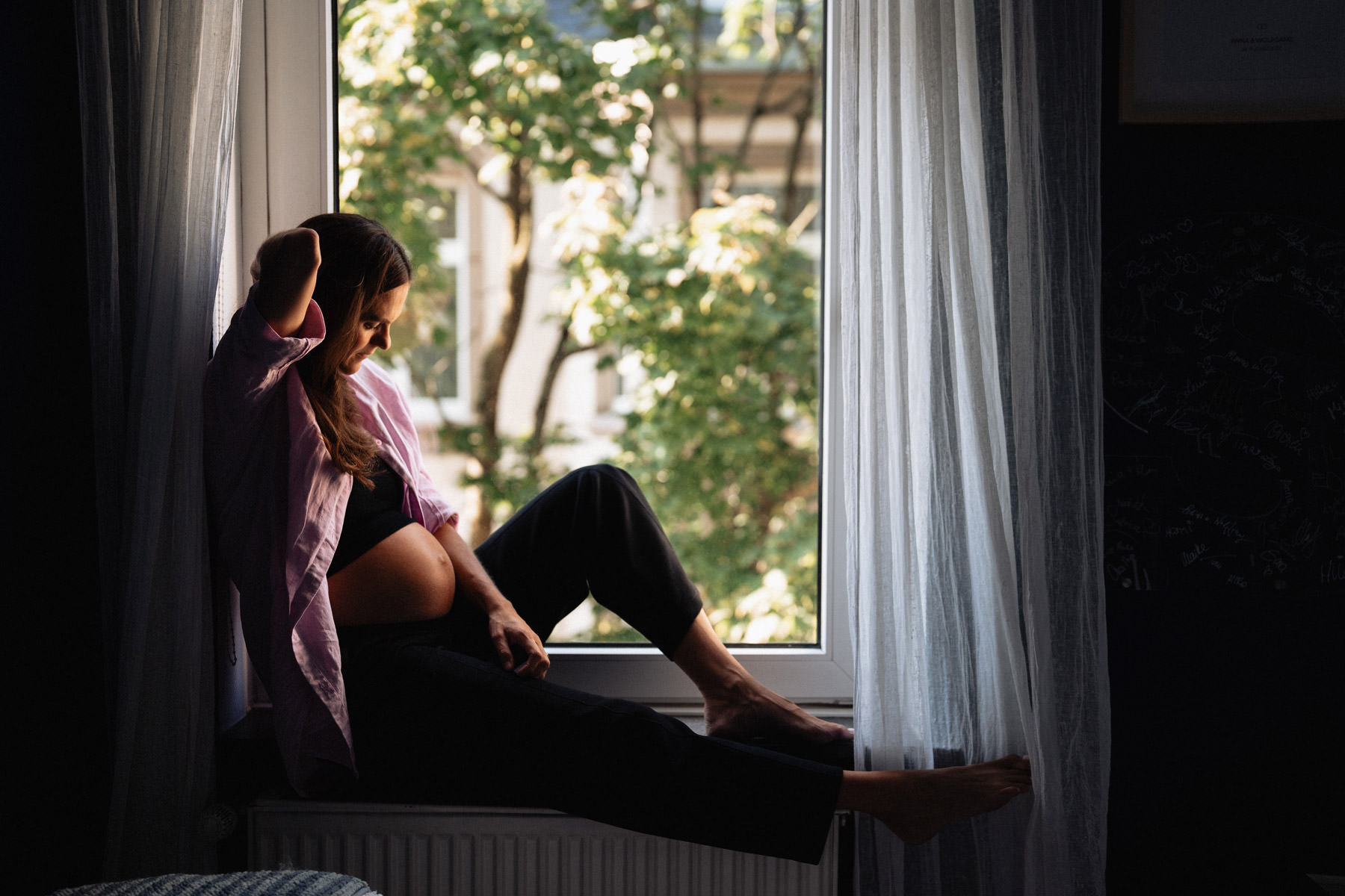 Schwangere Frau sitzt entspannt am Fenster, ruhige Szene mit viel Raum