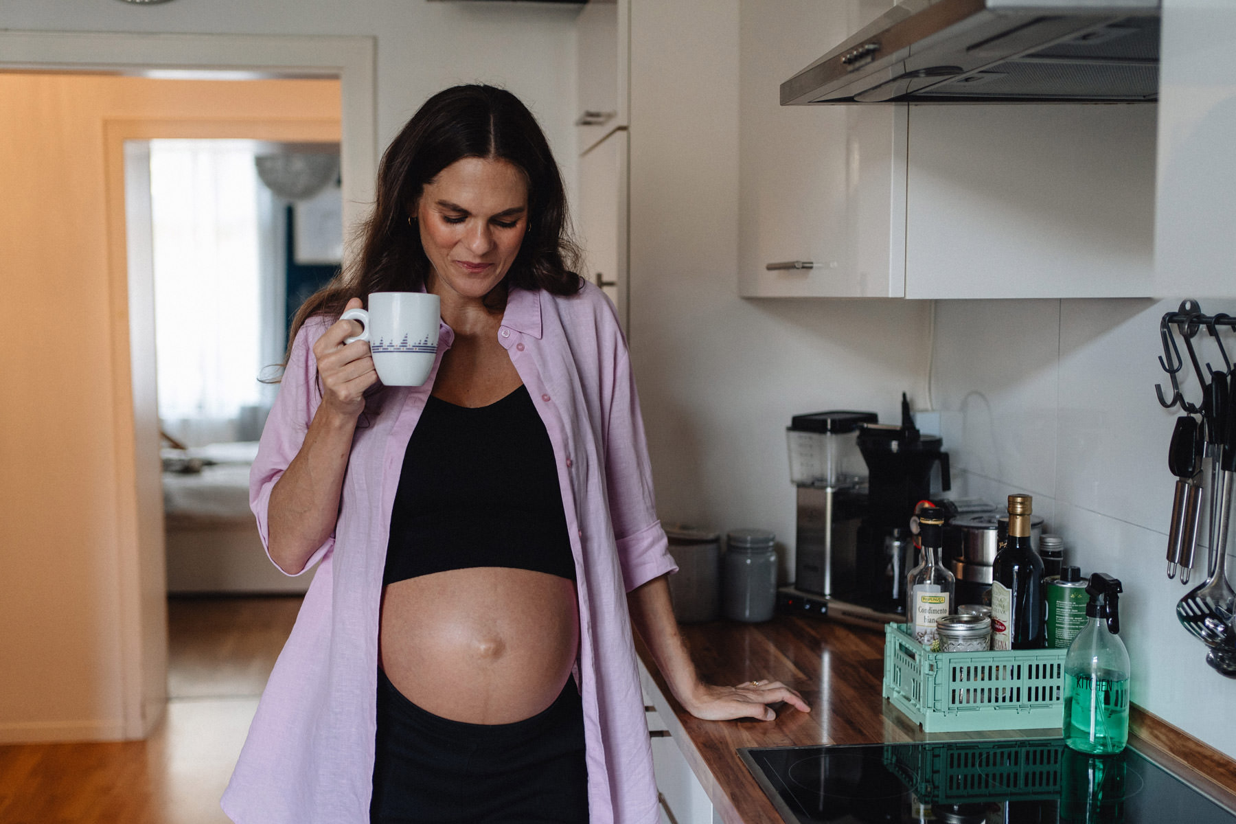 Schwangere Frau steht in der Küche mit einer Kaffeetasse, ruhiger Alltagsmoment