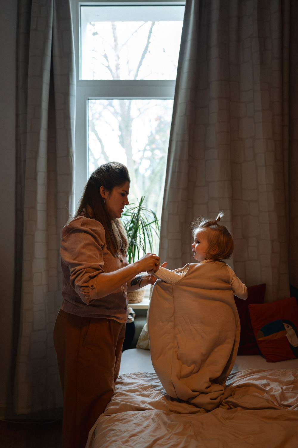 Mutter zieht Kind im Schlafzimmer den Schlafsack für den Mittagsschlaf an. Im Stehen auf dem Bett