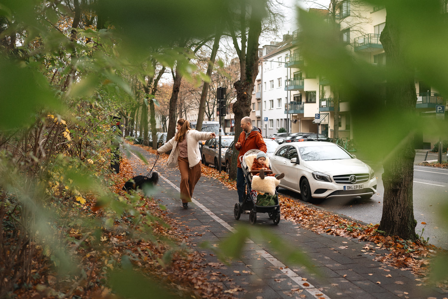 Familie geht mit Kind und Hund spazieren. Der Hund zieht die Mutter ins Gebüsch