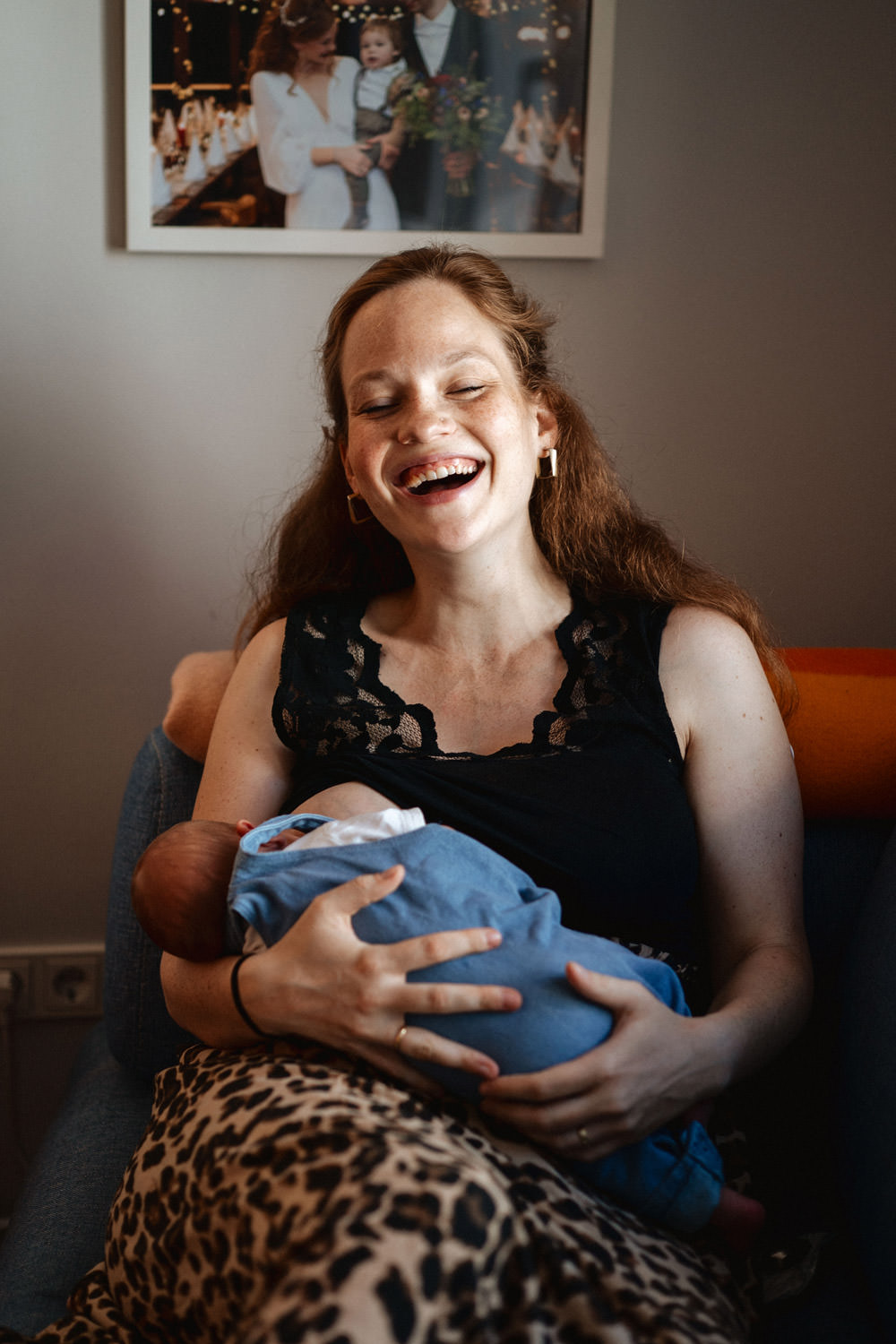 Mutter sitzt auf dem Sofa und stillt ihr Baby und lacht und ist glücklich